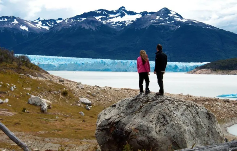 Dos personas observando el glaciar y las montañas desde un mirador natural, en la excursión Glaciar Sur